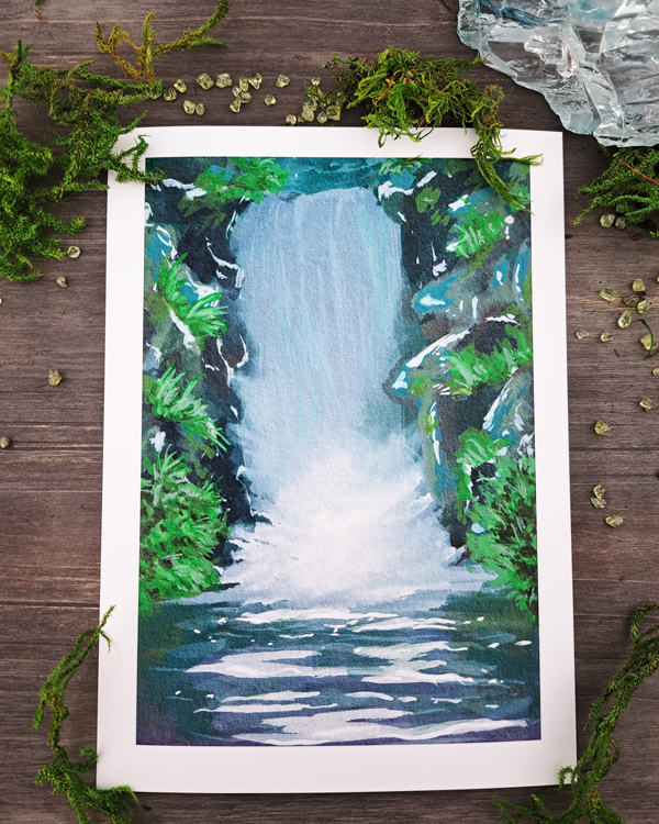 An image of a sticker surrounded by crystals and moss. The sticker features a vertical landscape with foliage and a waterfall, which was painted with acrylic inks.