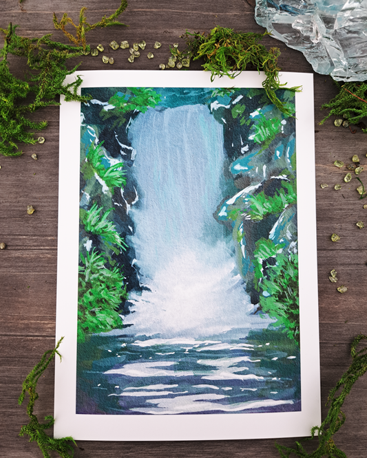 An image of a sticker surrounded by crystals and moss. The sticker features a vertical landscape with foliage and a waterfall, which was painted with acrylic inks.