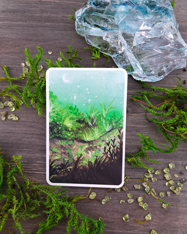 An image of a sticker surrounded by crystals and moss. The sticker features a vertical landscape with foliage along a pathway with a white moon shown in the pale blue sky, which was painted with acrylic inks.