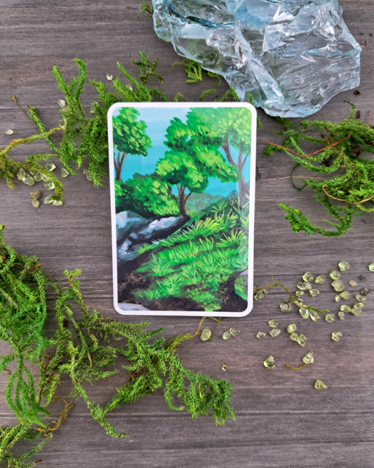 An image of a sticker surrounded by a crystals and moss. The sticker features a landscape with rocks, trees and grass, which was painted with acrylic inks.